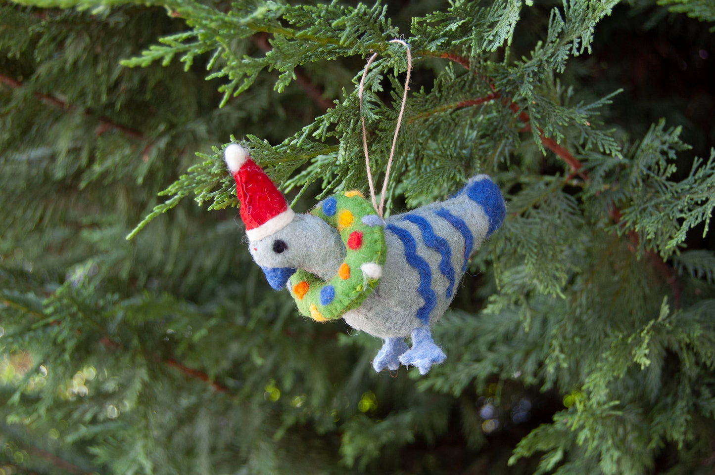 Felted pigeon ornament with a red Santa hat and colorful wreath hanging on a Christmas tree - ZWEIBIE