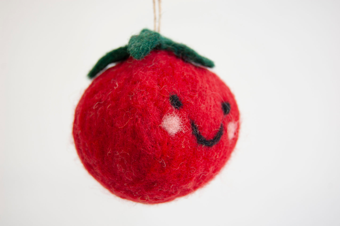 Red felt tomato ornament with a smiley face on a white background