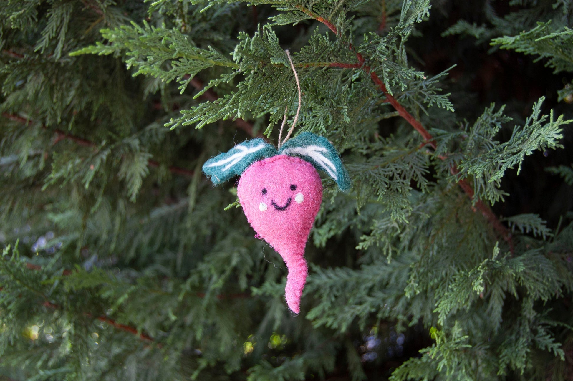 Pink decorative vegetable ornament with a face hanging on a Christmas tree.