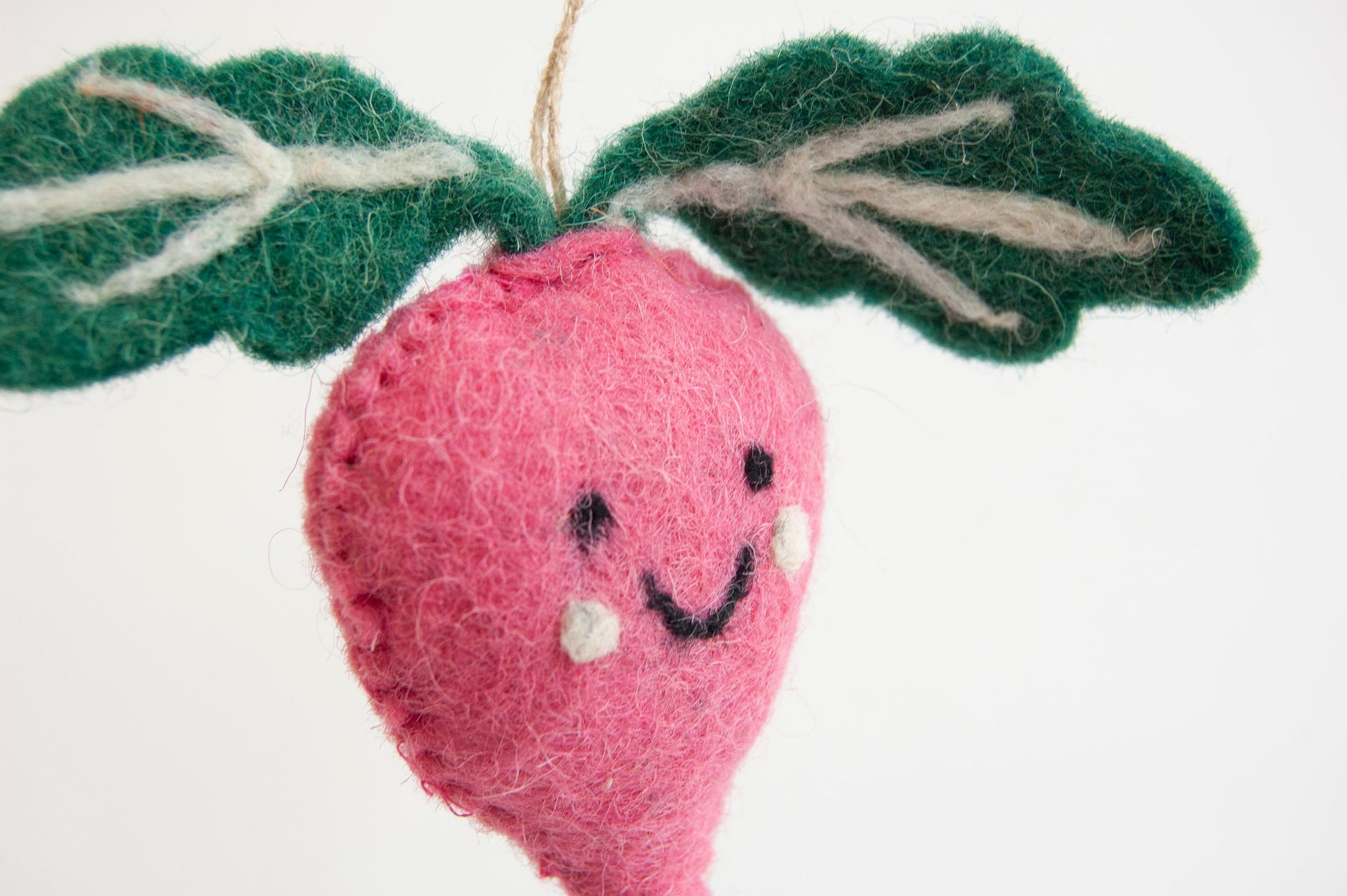 Felted pink radish ornament with green leaves on a white background