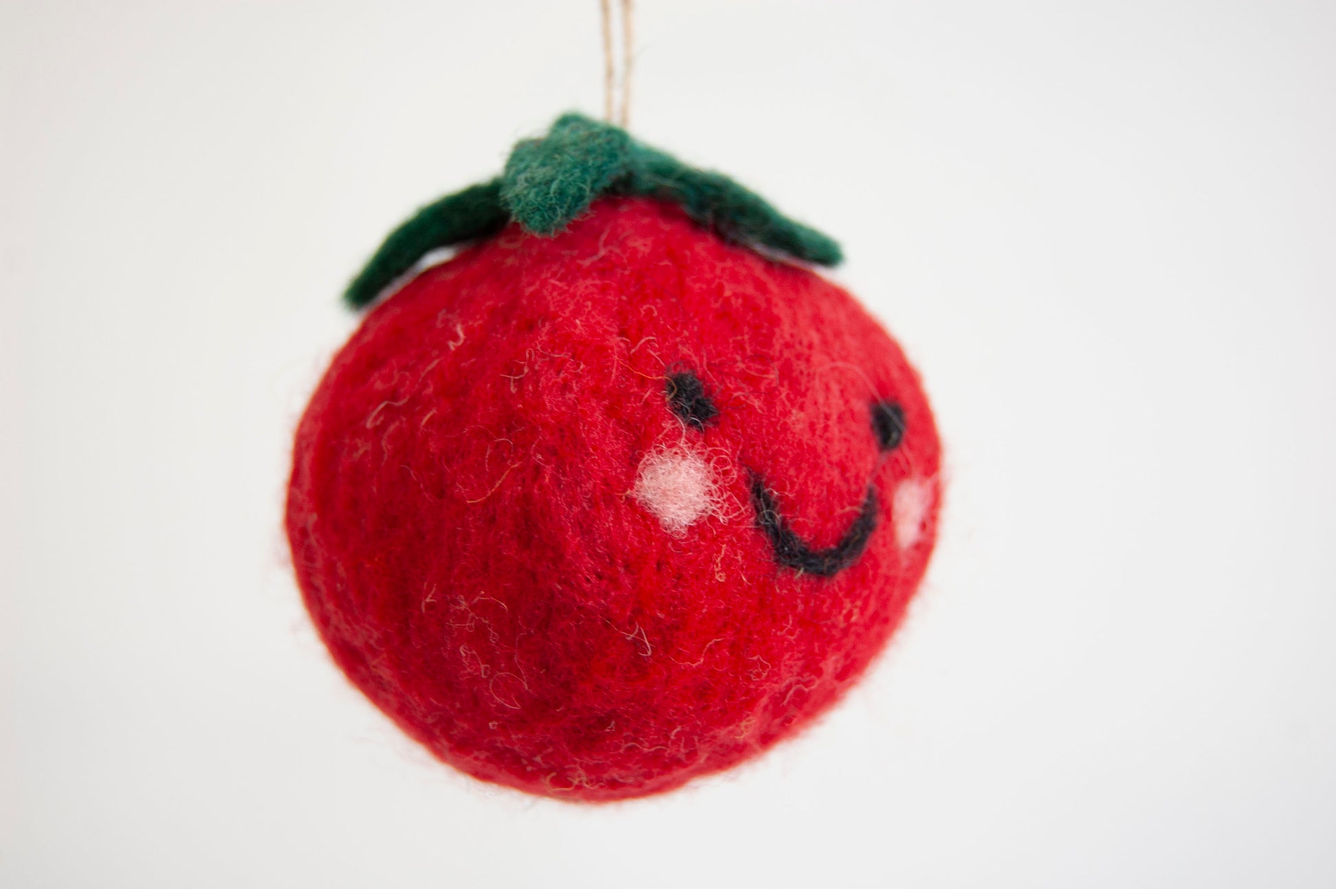 Red felt tomato ornament with a smiley face on a white background